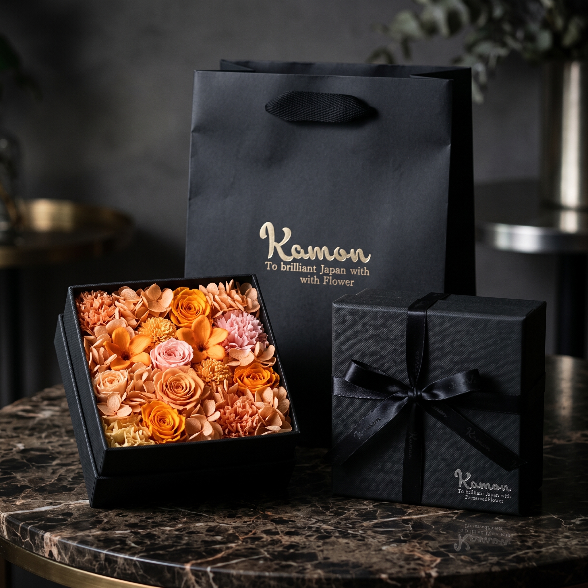 大理石のテーブルに置かれた、オレンジ系のプリザーブドフラワーのギフトボックスとKamonのショッパー|FLOWER KAMON